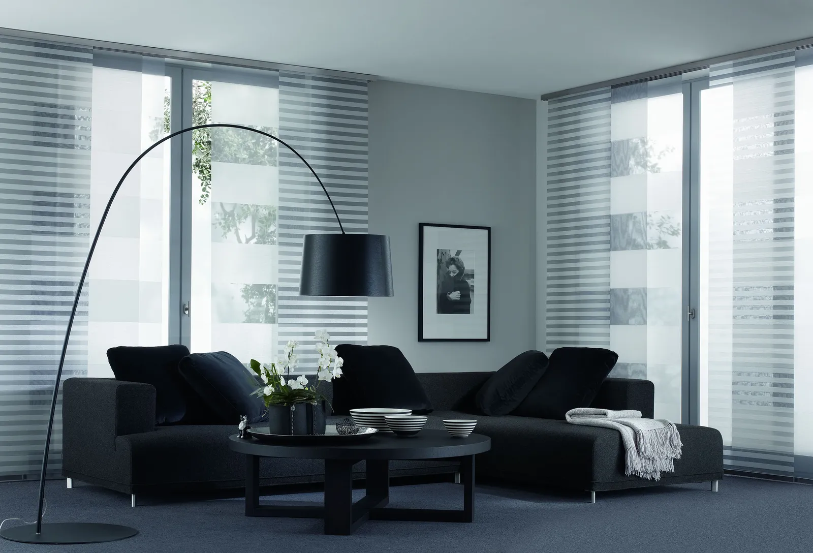 Wohnzimmer mit weiß gestreiften Flächenvorhängen und dunklem Sofa