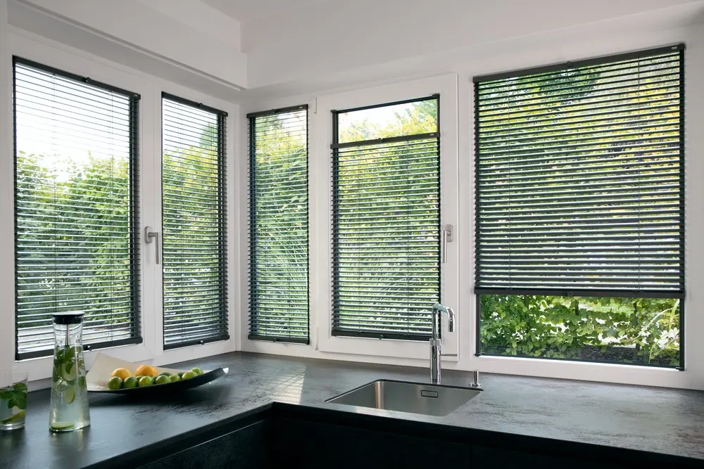 Küche mit dunklen Aluminium-Jalousien an fünf Fenstern über der Spüle