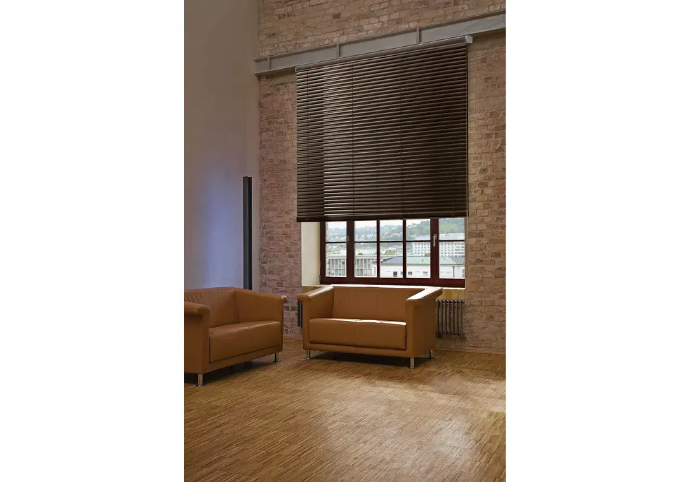 Dunkle Holzjalousie an einem hohen Fenster in einer Backsteinwand über einem Ledersofa