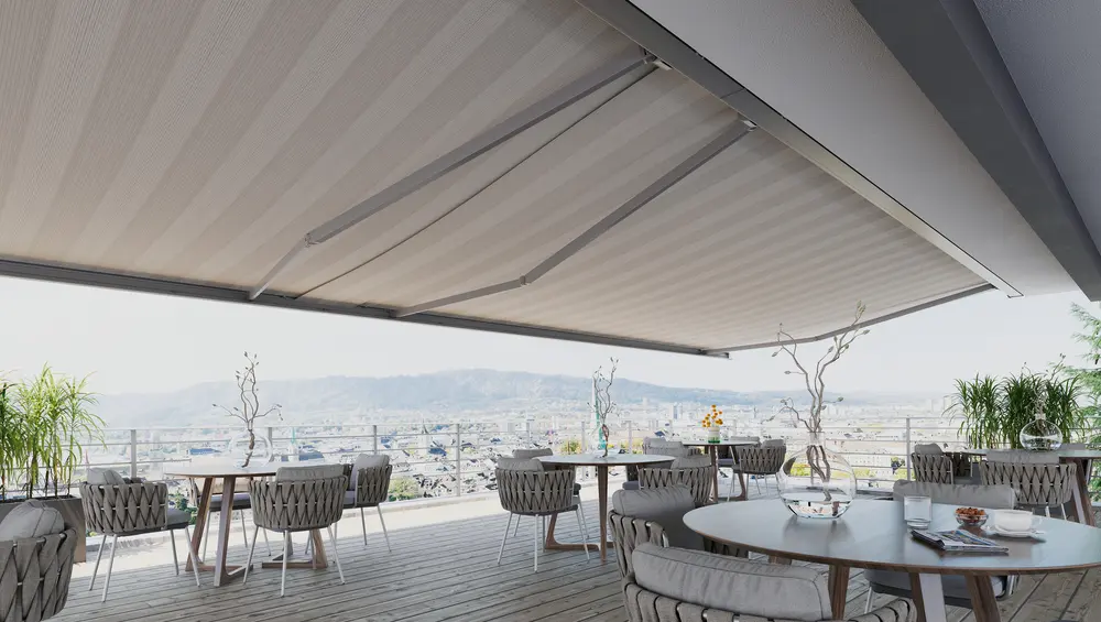 Große Markise mit hellem Streifentuch über einer Dachterrasse mit Tischen und Blick über die Stadt